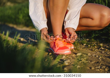 Female athlete lacing sport shoes before cross running and training over country road. Runner getting ready for outdoor challenge.