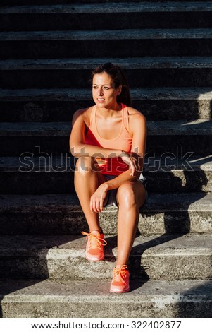 Relaxed woman taking a fitness workout rest sitting on stairs.  Motivation and healthy lifestyle concept.