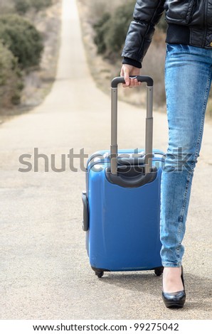 Woman leg in jeans. Travel and get away concept. Sexy female leg and suitcase on lonely road background.