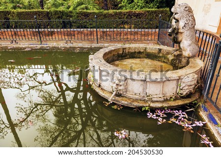 SEVILLE, SPAIN-OCTOBER 21, 2012 Lion Statue Fountain Pool Reflection Fish Flowers Garden Alcazar Royal Palace Seville  Andalusia Spain on October 21, 2012.  Oldest Royal Palace still in use in Europe.