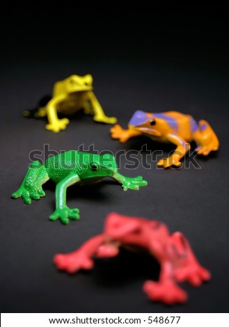 Toy frogs on a black background.  Selective depth of field makes the green frog stand out.