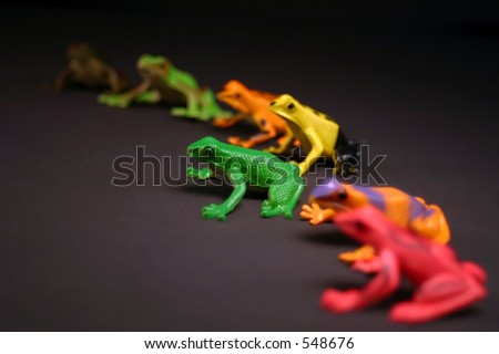 Toy frogs in a semi circle.  Selective depth, make the green frog stand out from the rest.