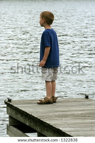 A boy standing on the edge of a pier looking into the distance.