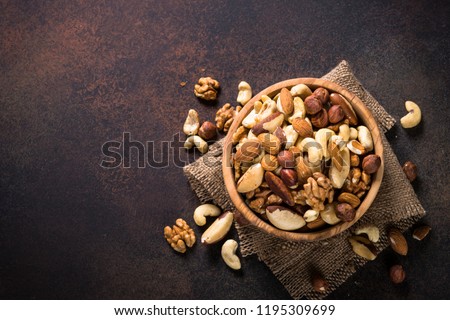 Assortment of nuts in wooden bowl on dark stone table. Cashew, hazelnuts, walnuts, almonds, brazilian nuts and pine nuts. Top view with copy space.