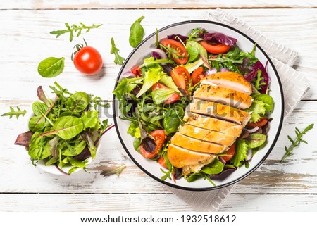 Green salad with baked chicken breast at white kitchen table. Healthy food, clean eating concept. Top view image.