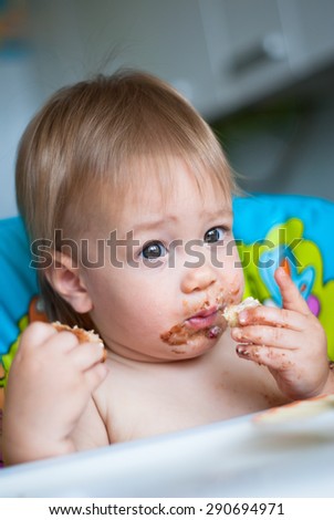 Child eats cake in the highchair. His face and hands smeared with cake