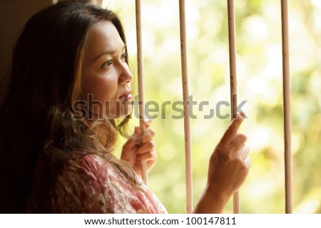 nostalgic sad woman holding window bars and looking outside