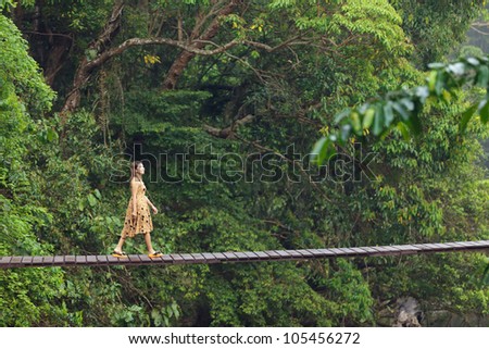 young woman walking on suspended wooden bridge in jungle, Thailand