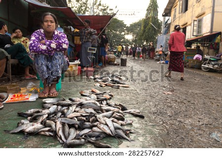 MANDALAY,MYANMAR,JANUARY 19, 2015: A woman is selling fresh fishes on the ground in a dirty and poor street market in Mandalay, Myanmar (Burma).