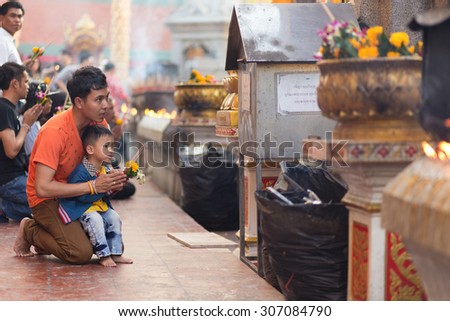 LAMPHUN, THAILAND, DECEMBER 31, 2014: A man and his son are praying for the new year outside the Buddhist temple of Wat Phra That Hariphunchai in Lamphun, Thailand