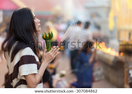 LAMPHUN, THAILAND, DECEMBER 31, 2014: A woman holding burning incense sticks and flowers is praying for the new year outside the Buddhist temple of Wat Phra That Hariphunchai in Lamphun, Thailand