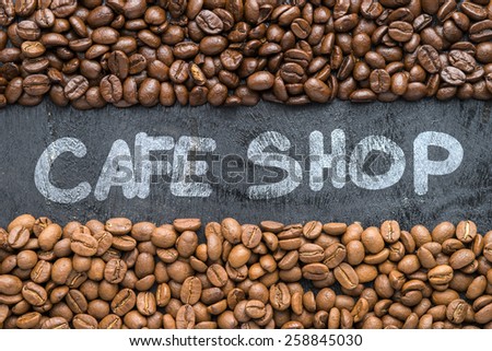 Coffee beans with Cafe Shop hand writing on black wooden background with blank space.
