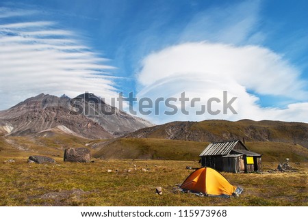 landscape consisting of a blue sky, clouds, mountains and yellow tent. Kamchatka located
