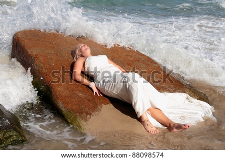 Bride laying on a rock as waves crash around her during trash the dress.