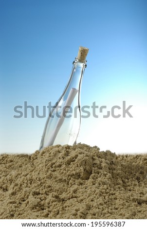 glass bottle with a rolled up paper in the sand