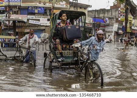 VARANASI, INDIA - AUGUST 11: Heavy monsoon rain causes a flash flood yet it\'s business as usual for this rickshaw and passenger despite the danger on August 11, 2011 in Varanasi, India.