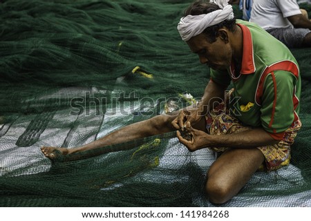 KANNUR, INDIA - NOVEMBER 27: Fisherman repairs a large deep sea fishing net by hand during inclement weather which prevented fishing on November 27, 2011 at Mapilla Bay harbour, Kannur, Kerala, India.
