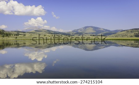 West Yellowstone, Wyoming, USA - Lake reflects trees, mountains, and clouds on a bring sunny day in Yellowstone National Park near West Yellowstone, Wyoming, USA.