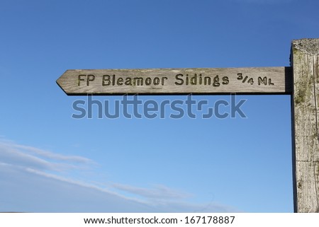 Wooden Public Footpath sign to Blea Moor Sidings on the Settle to Carlisle Railway against a clear blue sky.
