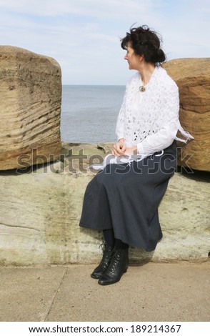 A woman in Edwardian dress sitting on Whitby Pier, looking out to sea.