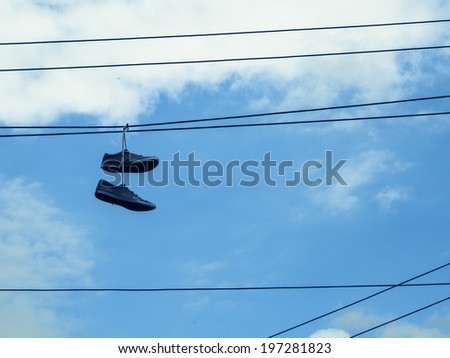 Pair of old sneakers hanging by their laces on a telephone wire