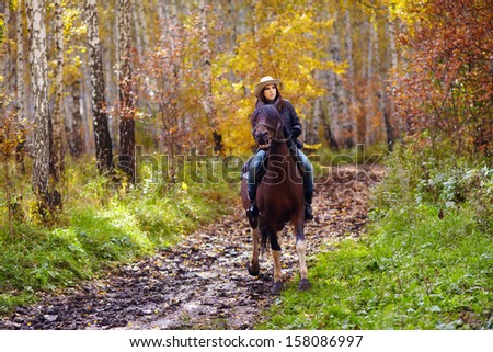 attractive woman in a hat riding a horse through the forest road