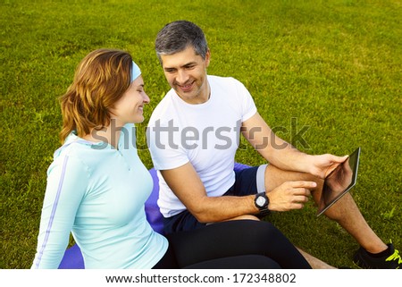 sports couple sitting on the grass using a digital tablet after training