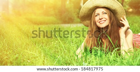 beautiful smiling dreaming woman in a hat lying on the grass in the summer sun and looks aside
