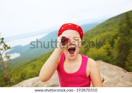 funny little girl in a bandana with a spyglass. children outdoors