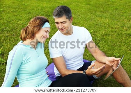sports couple sitting on the grass using a digital tablet after training. healthy lifestyle. outdoors