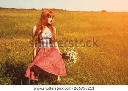 redhead woman with a bouquet of flowers in a dress outdoors. Beautiful stylish romantic young girl on nature background. field and clear cloudless sky