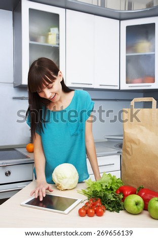 young housewife uses a tablet computer in the kitchen. woman following recipe cooking vegetables on digital tablet. online food shopping