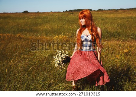 redhead woman with a bouquet of flowers in a dress outdoors. Beautiful stylish romantic young girl on nature background. field and clear cloudless sky
