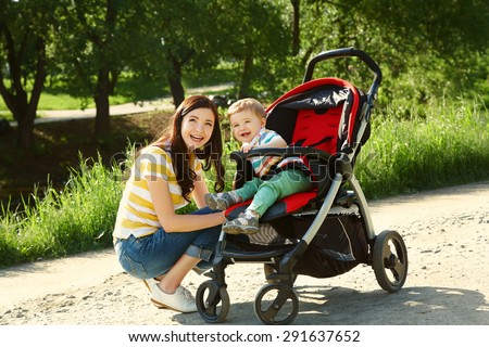 outdoor portrait of a happy mother and son. baby sitting in stroller and mom walk in the summer park