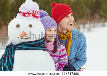 funny dad and daughter with a snowman. Family walking outdoors in winter
