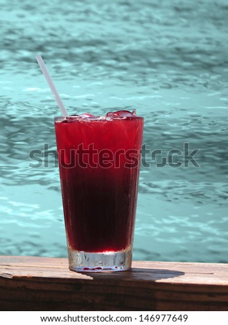 Red tropical drink by pool on warm summer day or on vacation