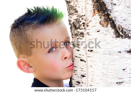 Young boy with blue and green spiky hair kissing a birch tree trunk
