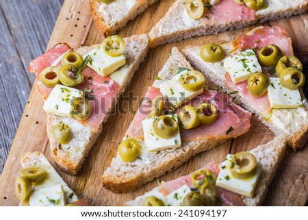 small sandwiches with bacon, goat cheese and pitted olives on old cutting board and wooden table