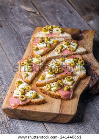 small sandwiches with bacon, goat cheese and pitted olives on old cutting board and wooden table