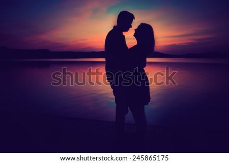Silhouettes of hugging couple against the lake at sunset. Vintage photo.