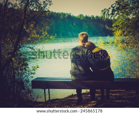 Silhouettes of hugging couple sitting on bench against the lake at sunset. Vintage photo.
