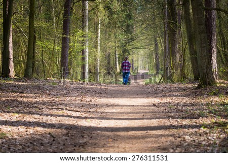 Mother with stroller walking by path in green springtime forest forest. Landscape with one person.