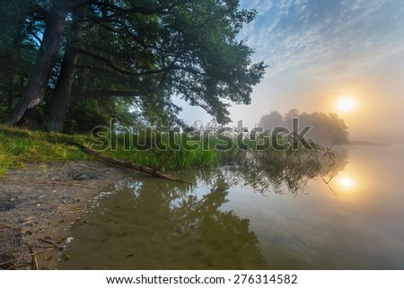 Beautiful sunrise over misty lake. Foggy morning over lake in Mazury lake district, Skanda lake near Olsztyn in Poland.