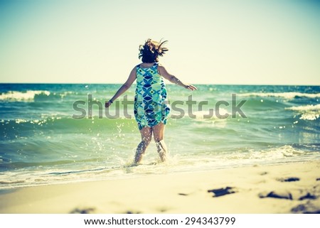 Woman jumping in water on sea shore with her legs in water. Summertime photo with vintage mood effect