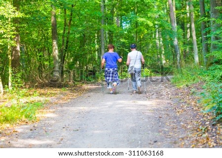 Two old womans nordic walking through forest path. Summertime forest with two ladies walking.
