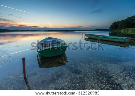 Fisherman boats moored on lake shore under sunset sky. Beautiful lake in Mazury lake district in Poland.
