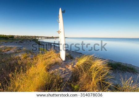White surfing board pounded in sand on sea shore with golden sunrise light. Beautiful landscape of polish sea shore