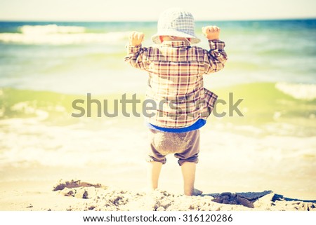 Little child playing on sea shore at good summer weather. Photo with vintage mood effect