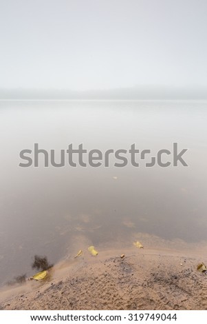 Shore of autumnal foggy lake. Beautiful polish landscape photographed in september at bad weather.