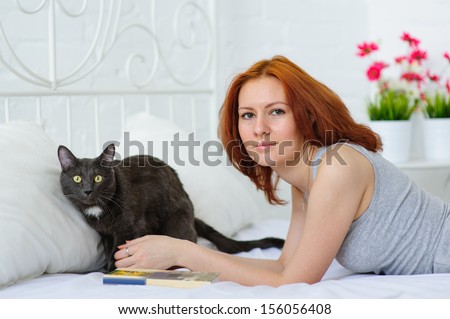 portrait of beautiful young brunette woman on the bed at home with her cat. Reading book